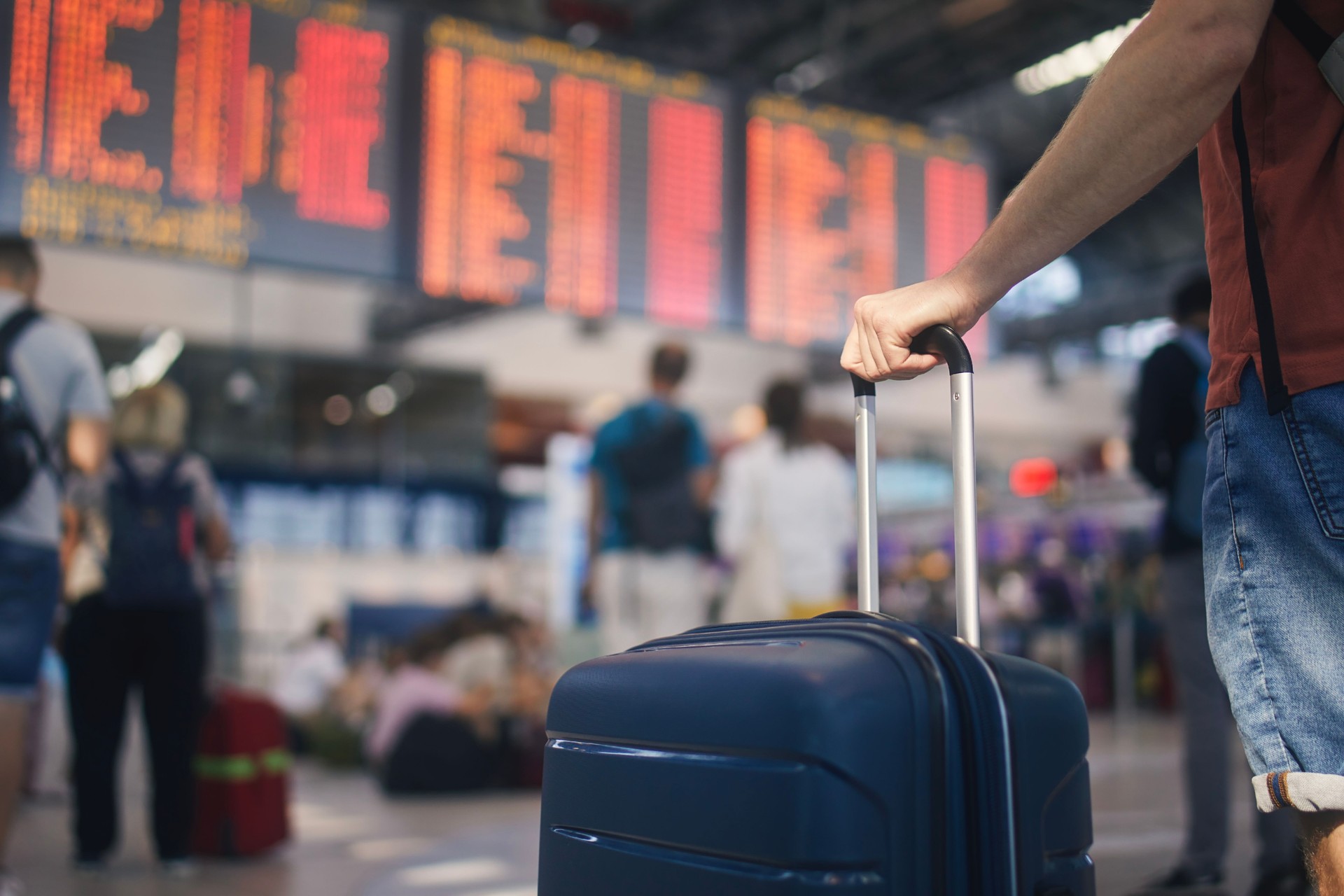 Mano dell'uomo mentre tiene la valigia contro il tabellone di arrivo e partenza all'aeroporto